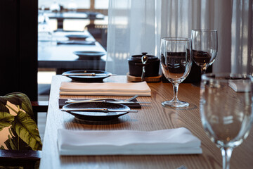 Elegant dining table set with black plates, white napkins, and wine glasses, showcasing a modern restaurant atmosphere with natural light and stylish decor