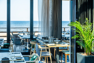 Modern restaurant interior featuring elegant dining tables, stylish chairs, and a stunning ocean view through large glass windows, creating a serene and inviting atmosphere for guests