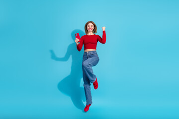 Obraz premium Charming young woman in stylish casual outfit celebrating joyfully with smartphone on vibrant blue background