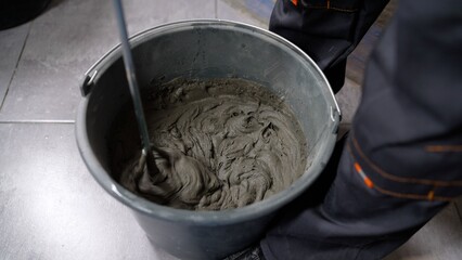 Worker mixing cement mortar in gray bucket