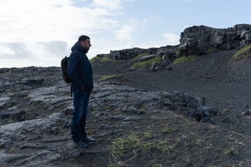 Fototapeta premium Man standing on rocky terrain, wearing a dark jacket, gazing at the landscape with a contemplative expression, surrounded by natural beauty and rugged textures