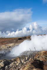 Volcanic landscape featuring steam rising from rocky terrain under a dramatic sky, showcasing geothermal activity and natural beauty in a unique environment