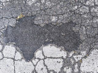 Cracked and damaged asphalt road surface with damp patch and distressed texture
