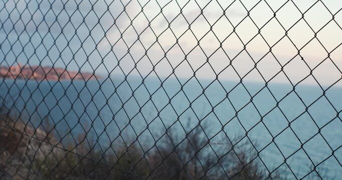 Coastal vista through chain link fence at sunset