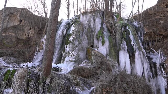 A frozen waterfall on a mountain river. The Bigar waterfall below Stara Planina is bound by ice, you can see ice stalactites and other ice forms, and some unfrozen water falling. The camera is static