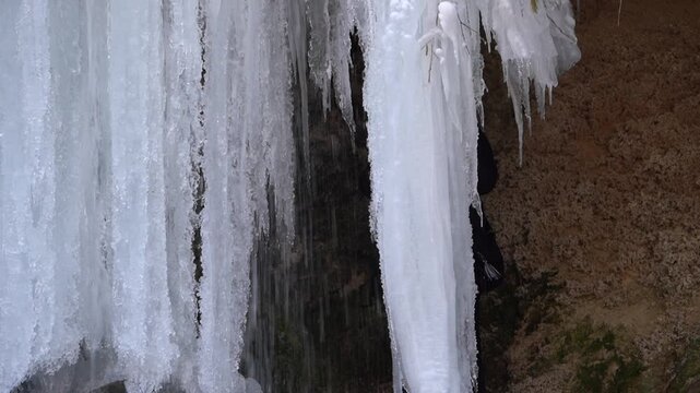 A frozen waterfall on a mountain river. The Bigar waterfall below Stara Planina is bound by ice. details of ice stalactites and other ice formations. Unfrozen falling water flows between the ice