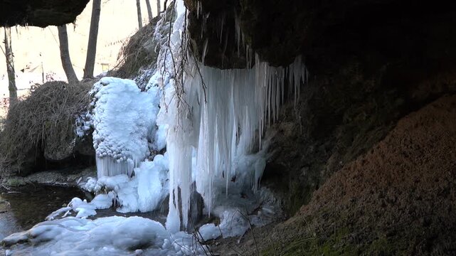  A frozen waterfall on a mountain river. The Bigar waterfall below Stara Planina is bound by ice. details of the icy stalactites Unfrozen falling water flows between the ice. Static shot.