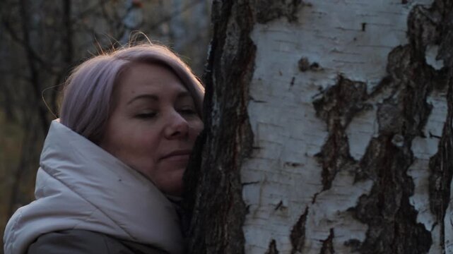 A happy Caucasian woman, 45 years old, hugs a tree in a forest or park, the concept of the unity of man with nature, a woman walking in the forest in autumn