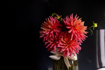 Bouquet of dahlias in green glass vase on dark background with sunlight.Vase of autumn flowers stands on table.Concept: greeting card, autumn holidays. Selective focus. Copy space