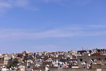 The cityscape of a Moroccan town shows rows of buildings with many satellite dishes on rooftops. This setting captures everyday life against a clear blue sky