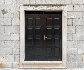Old bivalve doors made of dark lacquered tree in a stone wall