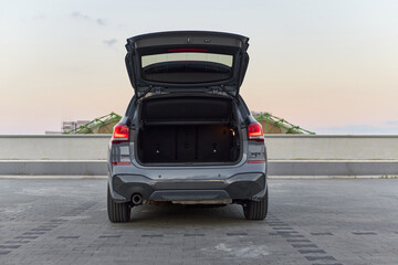 A modern SUV is parked on a rooftop at sunset, showcasing its open trunk. The spacious storage area is empty, and the horizon is lit with soft evening colors