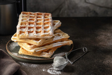 Delicious belgian waffles in stack with powdered sugar on a plate on dark background, text space