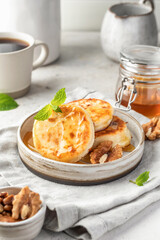 Cottage cheese pancakes or syrniki with walnuts and honey on ceramic plate on light gray kitchen table. Healthy sweet breakfast