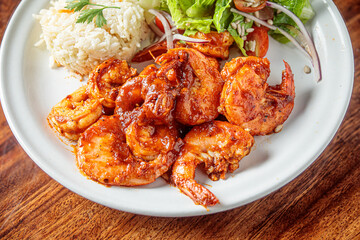A plate of camarones a la diabla, spicy shrimp cooked in a rich red sauce, served with white rice and a side salad.