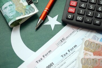 Pakistan rupees banknotes with calculator and tax form. The current Pakistan real money bills and tax blank close up. The concept taxpaying and accounting in Pakistan