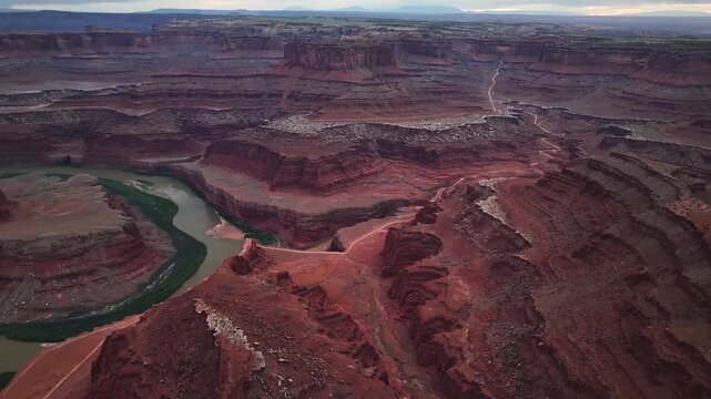 Aerial view of deep canyons carved by a winding river, showcasing contrasting red rock formations and sparse greenery, Moab, Utah, United States.