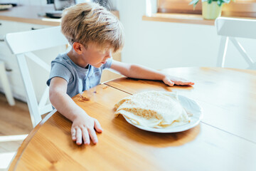 Little boy sitting at kitchen table waiting for pancakes on plate