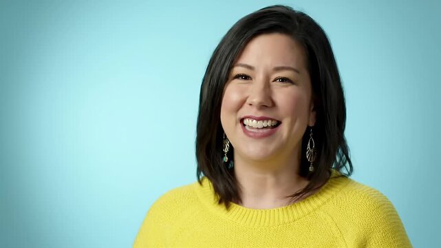 Joyful Young Woman Laughing with Genuine Happiness Against a Soft Blue Background - Portrait of a Smiling Asian Female in Yellow Sweater Expressing Positive Emo