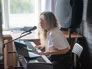 Caucasian woman singing into microphone and playing synthesizer. 