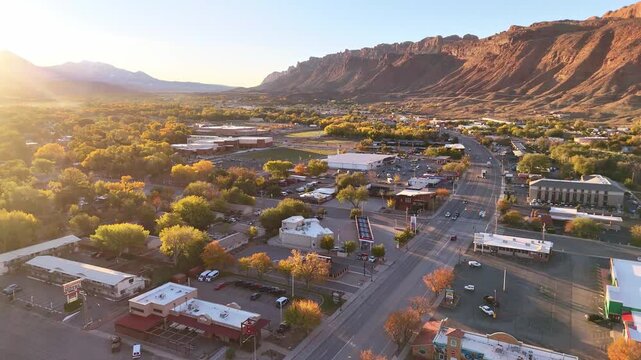 Moab, United States - 07 November 2024: Aerial view of the city nestled among red rock formations, bathed in soft sunlight, showcasing autumn foliage and urban landscape.