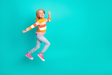 Happy girl jumping cheerfully in stylish striped sweater and jeans with vibrant turquoise background