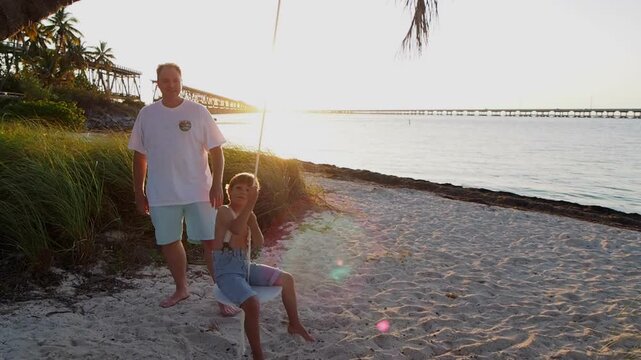 Father Pushing Son on Rope Swing at Sunset on the Beach in the Florida Keys