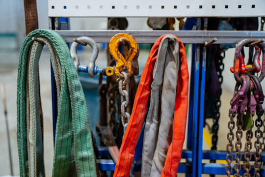 Industrial lifting straps, chains, and hooks organized on rack in mechanical workshop representing heavy load handling equipment, safety-certified rigging tools, and professional lifting technology