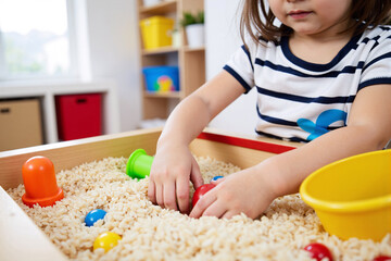 Young child playing with toys in sensory sand table at preschool or daycare. Concept of early childhood development, hands-on learning, and sensory play for toddlers in kindergarten