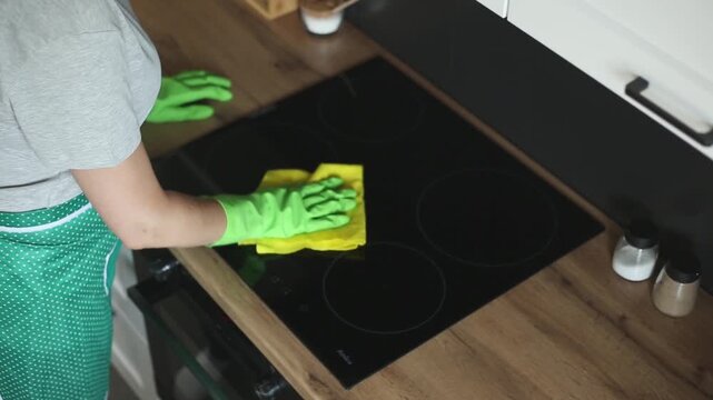 Woman with green rubber gloves is cleaning a kitchen
