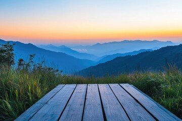 A serene view of layered blue mountains at dawn or dusk, from a rustic wooden deck amidst vibrant green grass.