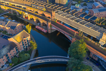 Sunrise aerial of Castlefield viaducts in Manchester showing yellow tram over Bridgewater Canal and moored boats.
