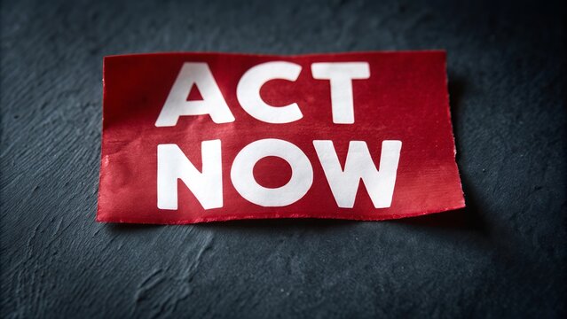 A red paper with the words act now in white lettering on a dark textured surface photographed closely