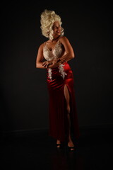 Full length portrait of beautiful woman in a red evening dress and a white wig on a black background