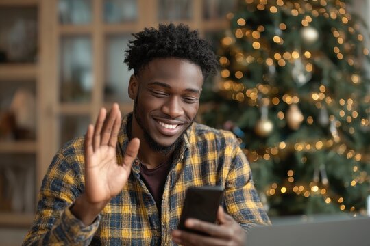 A young Black man video chatting by a Christmas tree at home