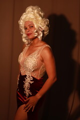 Beautiful woman in a red evening dress and a white wig against a background of brown curtains