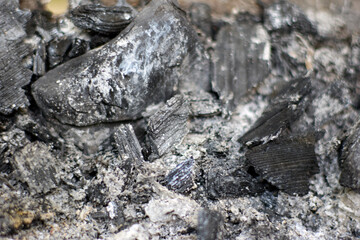 An up-close perspective of black and gray charcoal mixed with ash, highlighting the detailed textures of burned wood remains and ash to create a natural monochrome view.