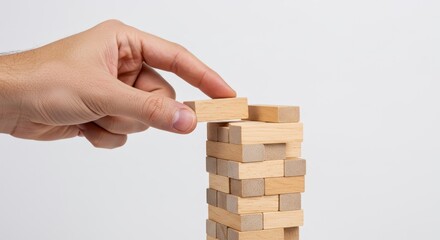 Close-up of a hand carefully placing a wooden block atop a precarious Jenga tower against a clean white background.