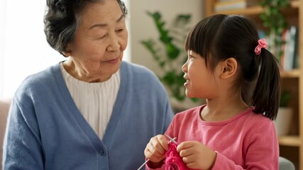 Grandmother teaching her granddaughter to knit with pink yarn in a cozy living room - Powered by Adobe