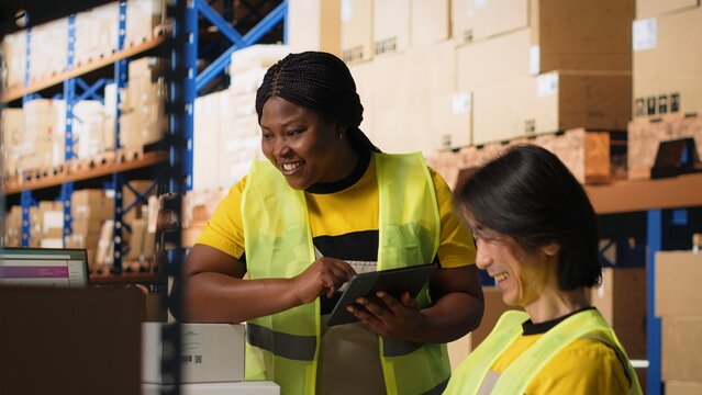 Satisfied coworkers sharing a high five after successful order processing, feeling proud of their teamwork in the industrial retail facility. Fulfillment center employees in workwear. Camera B.