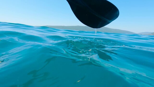 Kayaker paddling in turquoise water. Turquoise water splashes gently as a kayaker propels forward, the paddle rhythmically dipping beneath the surface, creating patterns of droplets and ripples