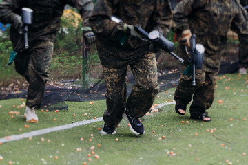 Paintball game, team in camouflage protective uniform with paintball guns and ammunition, strikeball arena battlefield, paintballer aiming and shooting at opponents, airsoft players match tournament