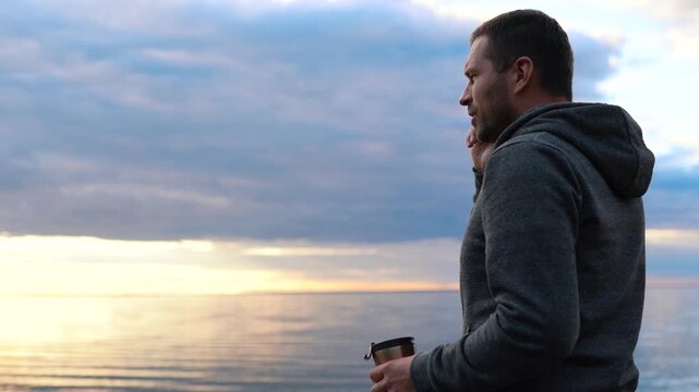 Man Speaks on the phone on a spacious coast near the sea or ocean. Sunset in the water.
