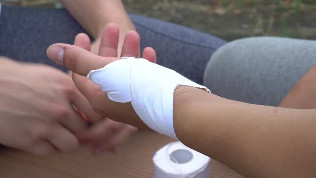 Outdoors two caucasian men do first aid. Close up, arms, fingers. First help of arm injury, man bandages another man's arm.