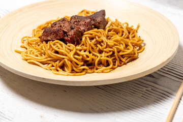 Sliced Steak on Soy-Sauce Noodles on a Wooden Plate
