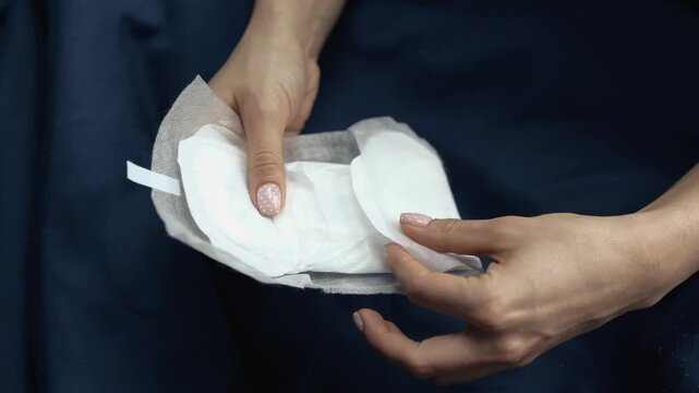 Picture of woman's hand holding female gasket for hygeine. Semi opened. Hold with both hands. Menstruation and pms period.