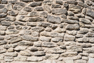 Old stone wall texture with rough uneven surface and natural beige color. Rough textured stone wall made of natural rocks and mortar