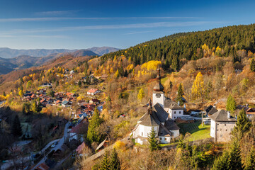 The Spania Dolina village in Slovakia, Europe. Picturesque village with historic church nestled in colorful autumn hills under a bright blue sky, evoking tranquility and timeless beauty.