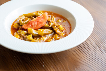 Close-Up of Traditional Okra Dish with Tomatoes on a White Plate on a Wooden Table
