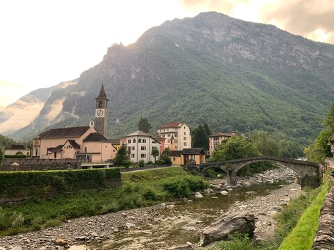 Bignasco - Ortschaft in der Gemeinde Cevio im Maggiatal, Kanton Tessin - Schweiz. Bild: Steinbr&uuml;cke, Fluss Maggia und Kirche im Abendlicht